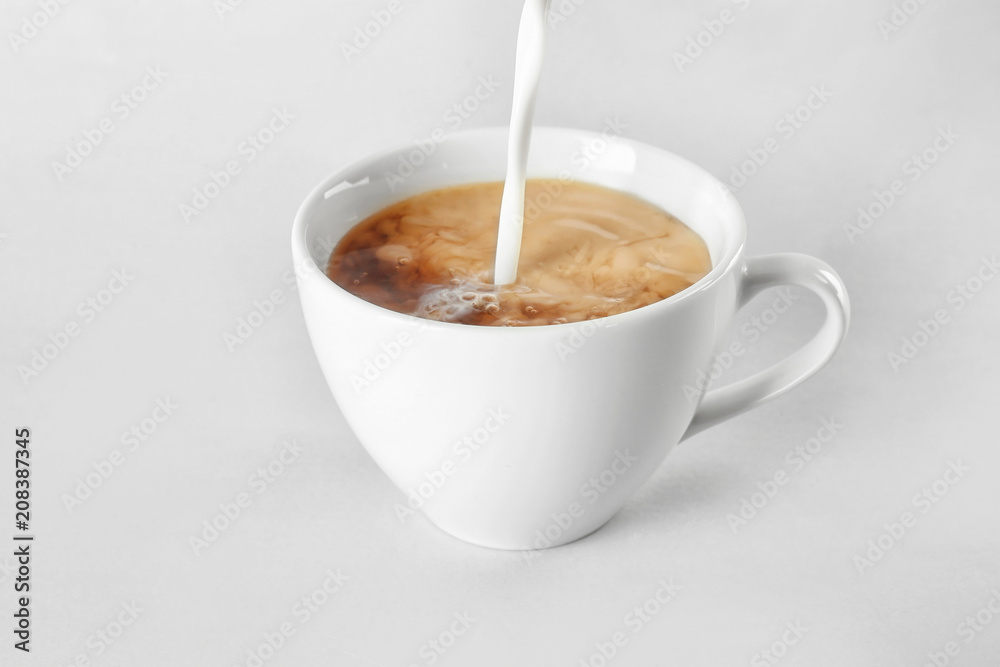 Adding milk to delicious tea on light background