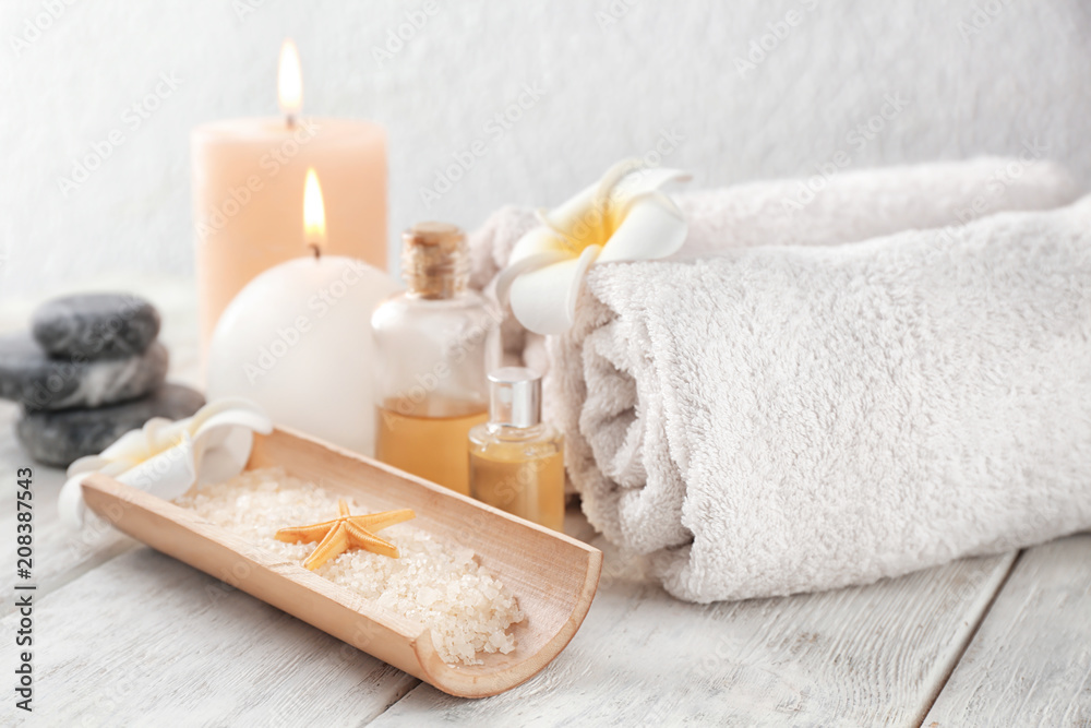 Spa composition with sea salt, candles and rolled towels on light background