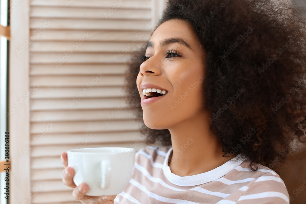 Beautiful African-American woman drinking tea indoors