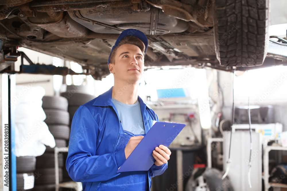 Male mechanic with clipboard examining car in service center