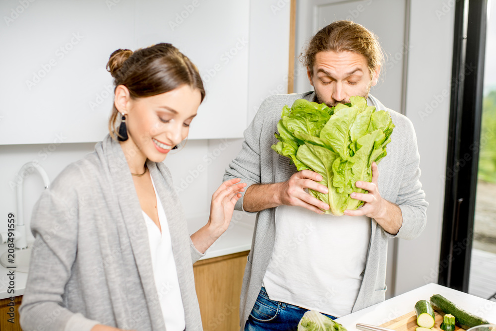 一对年轻快乐的夫妇穿着灰色毛衣，在现代厨房里烹饪蔬菜