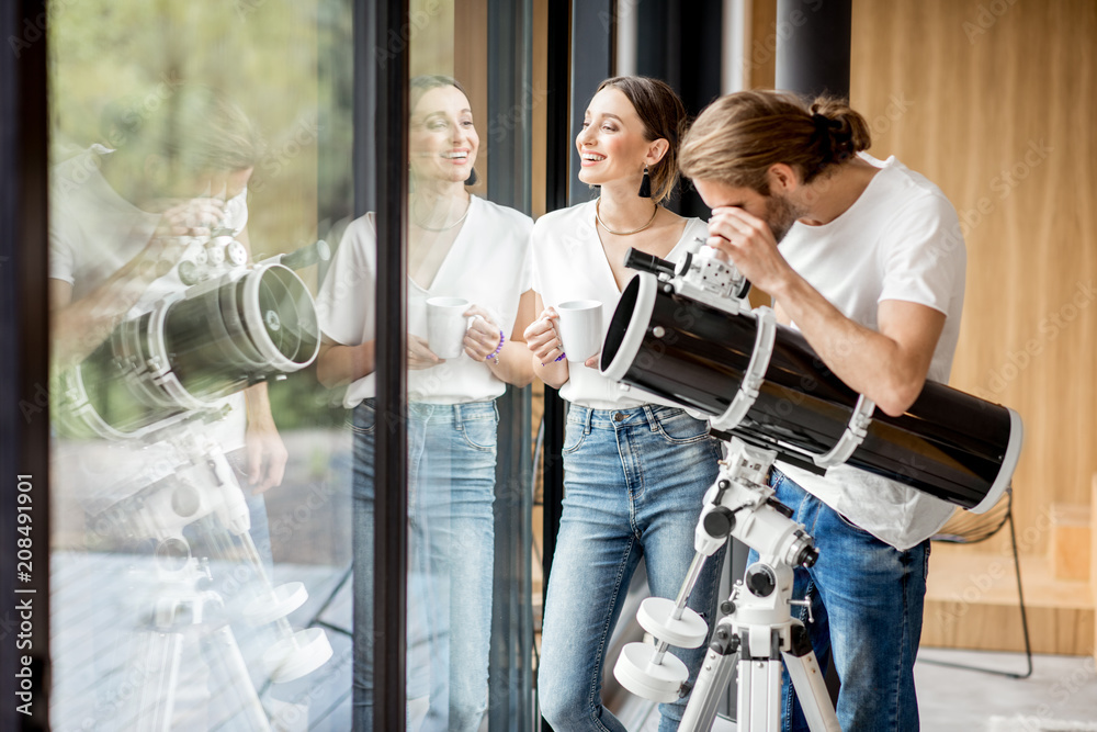 Young couple watching with telescope standing near the window in the modern house