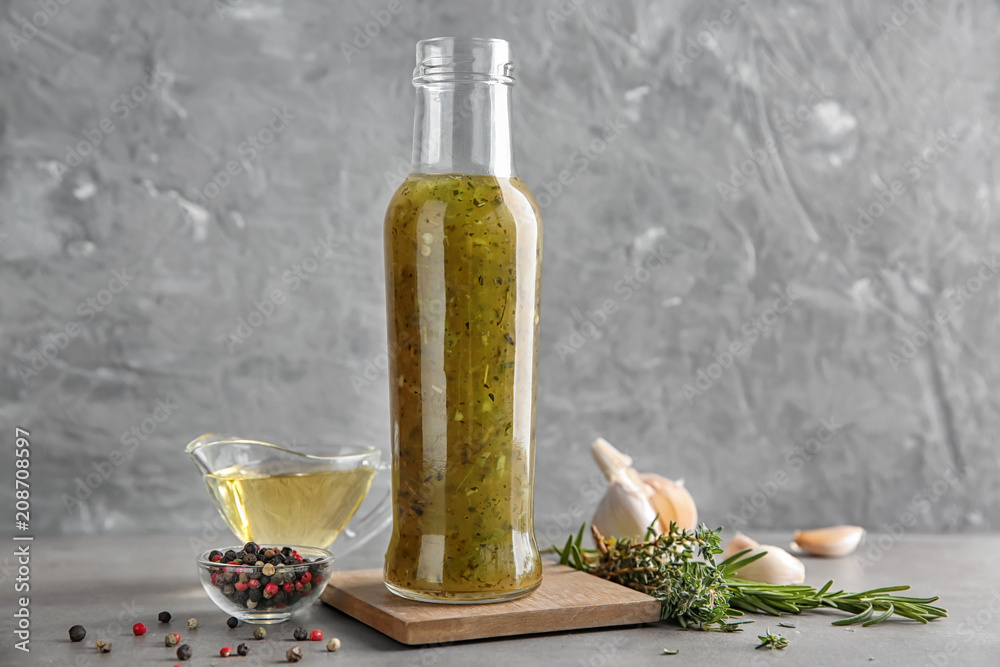 Bottle with tasty green sauce and herbs on table