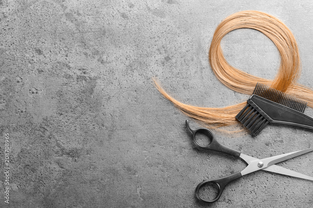 Flat lay composition with hairdressers tools and strand of blonde hair on grey background