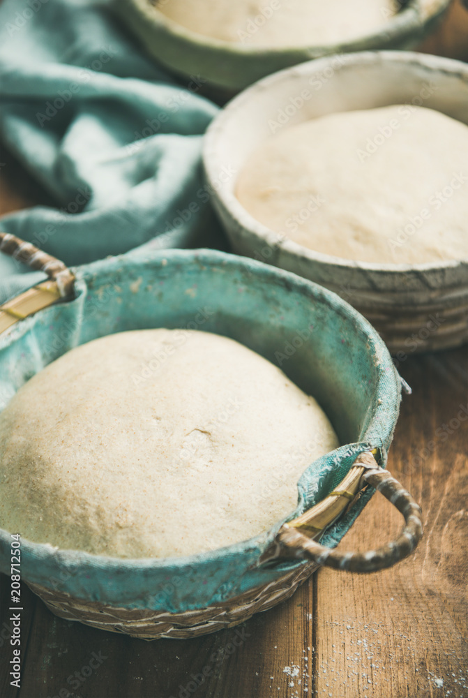 在质朴的木制厨房餐桌背景下，在篮子里烤自制小麦面面包的Sourdough