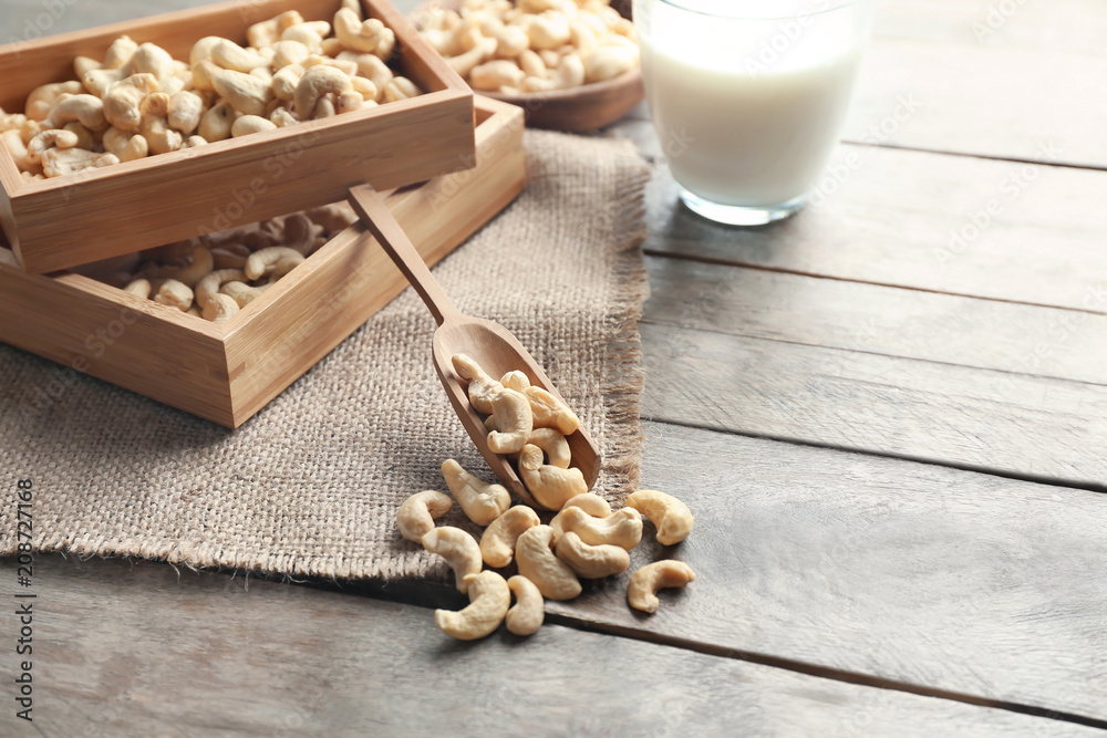 Wooden boxes with tasty cashew nuts and scoop on wooden table