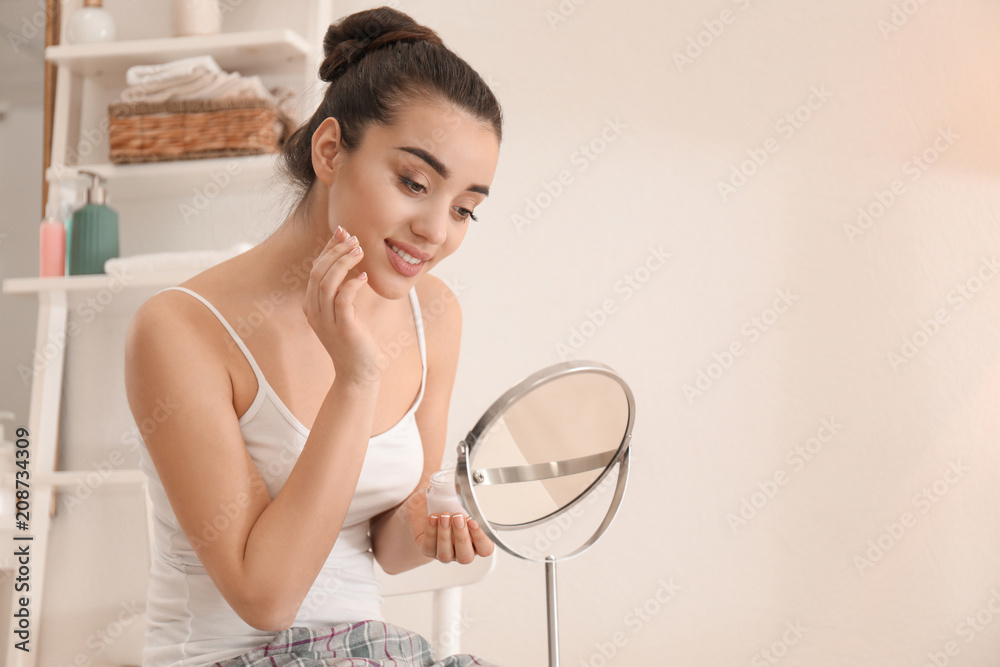 Young woman applying face cream in morning