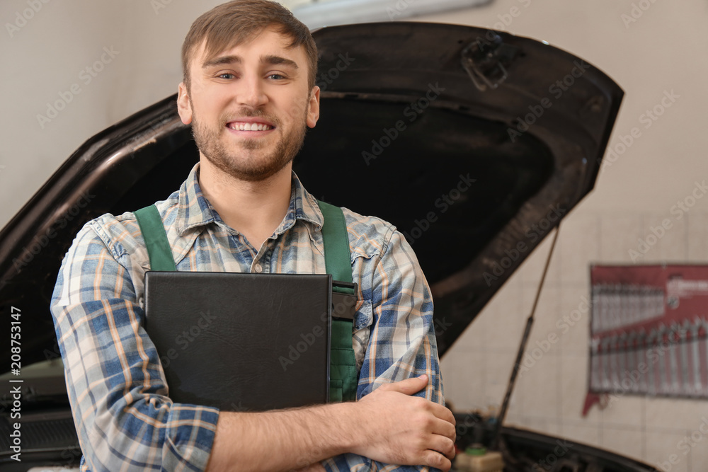 Young auto mechanic with clipboard near car in service center