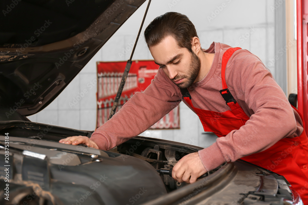 Young auto mechanic repairing car in service center