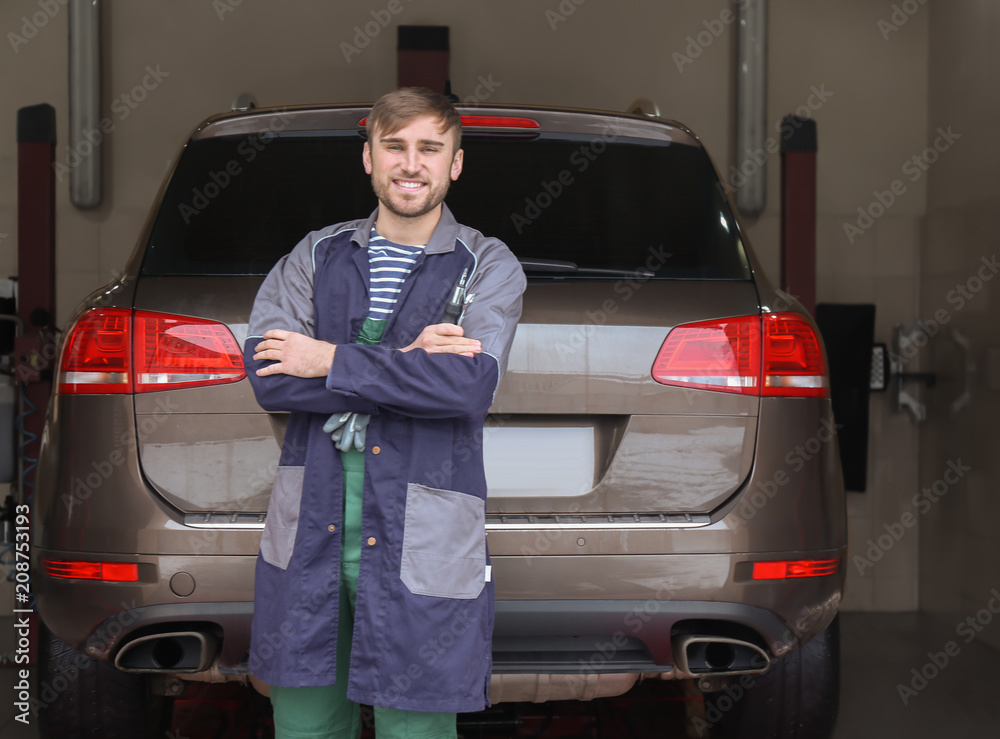 Young auto mechanic with tools near car in service center