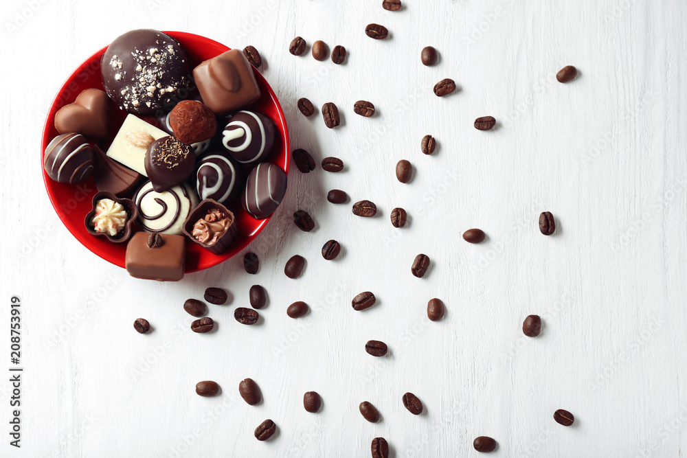 Plate with tasty chocolate candies and coffee beans on wooden table