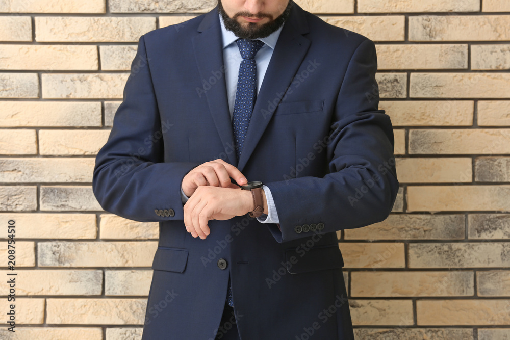 Man looking at his watch on brick background. Time management concept