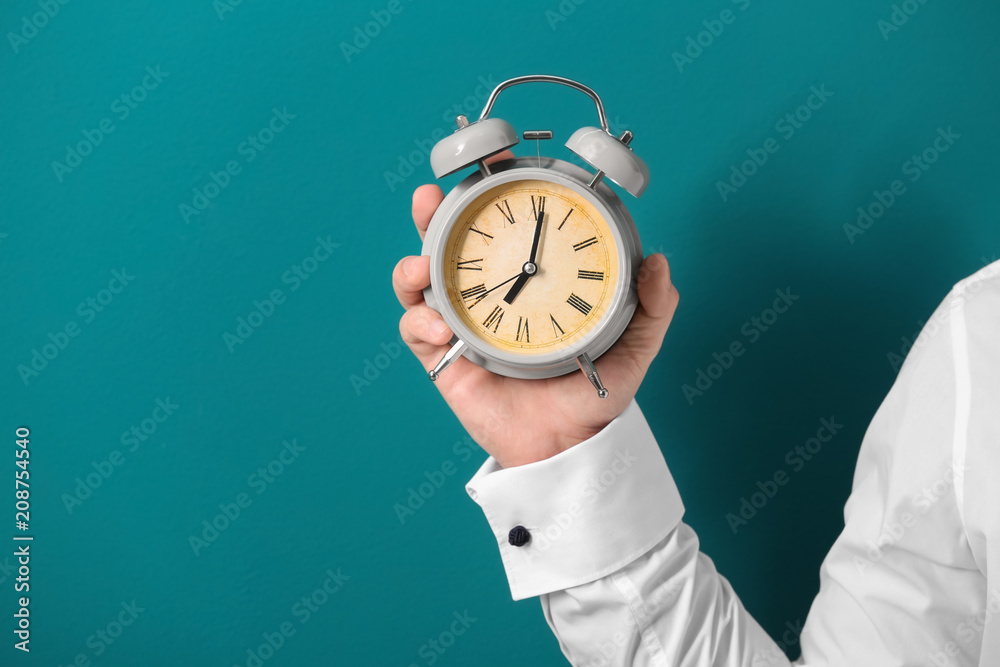 Man holding alarm clock on color background. Time management concept