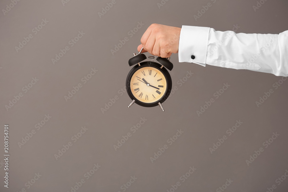 Man holding alarm clock on gray background. Time management concept