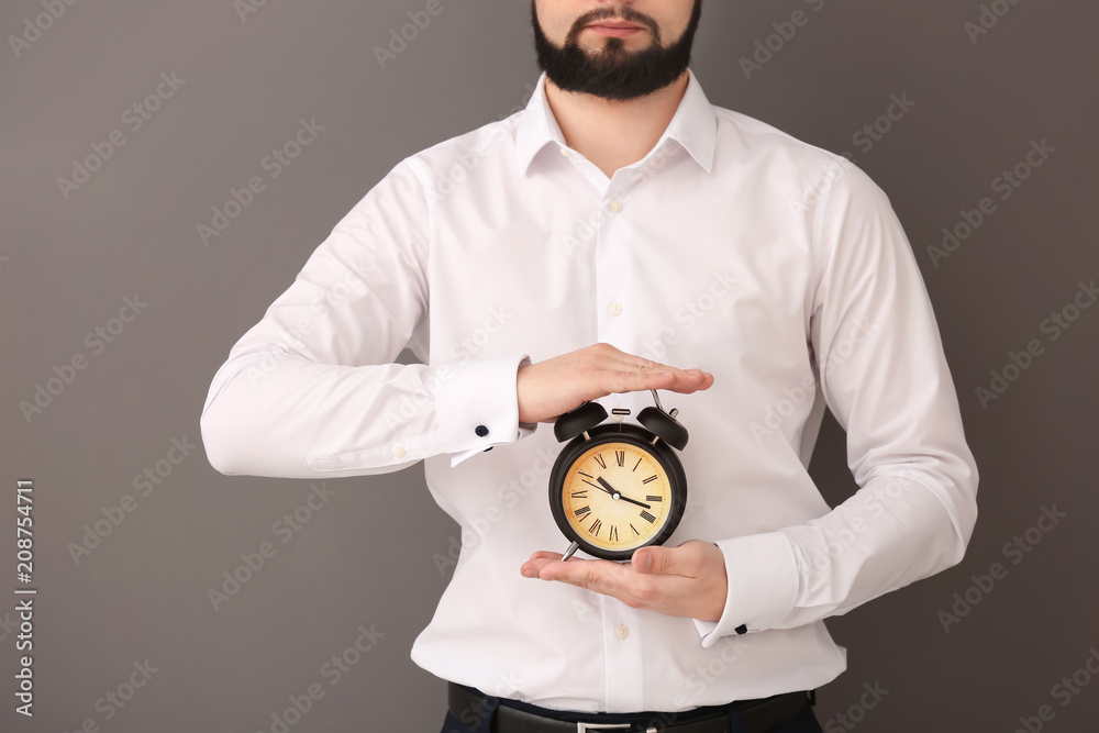 Man holding alarm clock on gray background. Time management concept