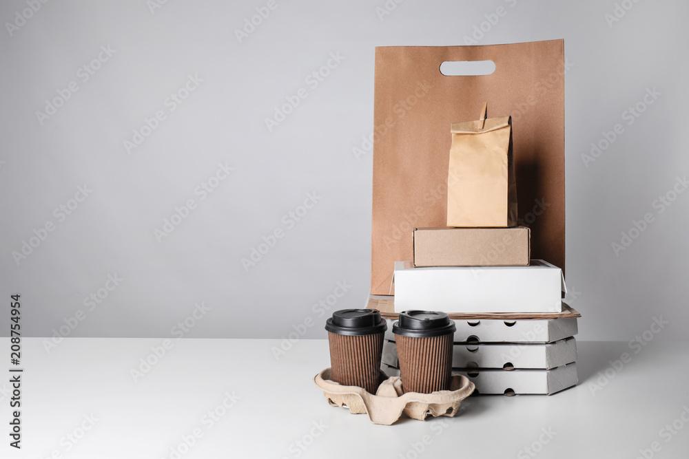 Different packages and carton cups on table against color background. Food delivery service