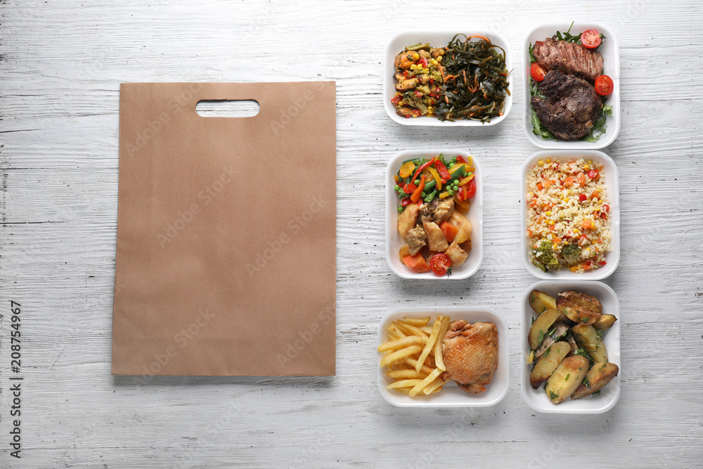 Plastic containers with delicious food and paper bag on wooden table. Delivery service