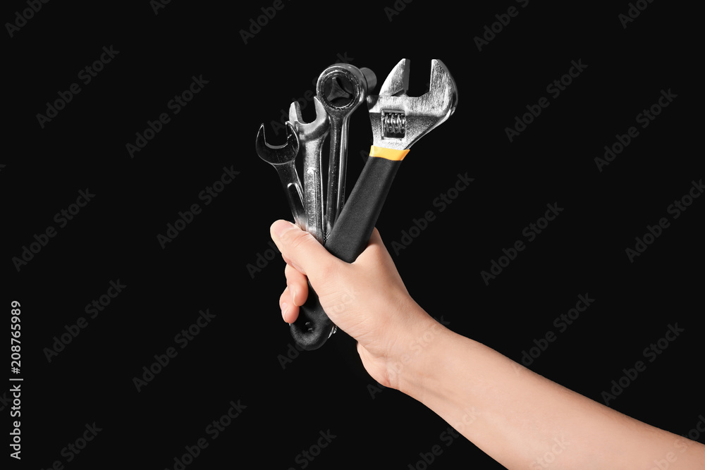 Female mechanic holding instruments on black background, closeup