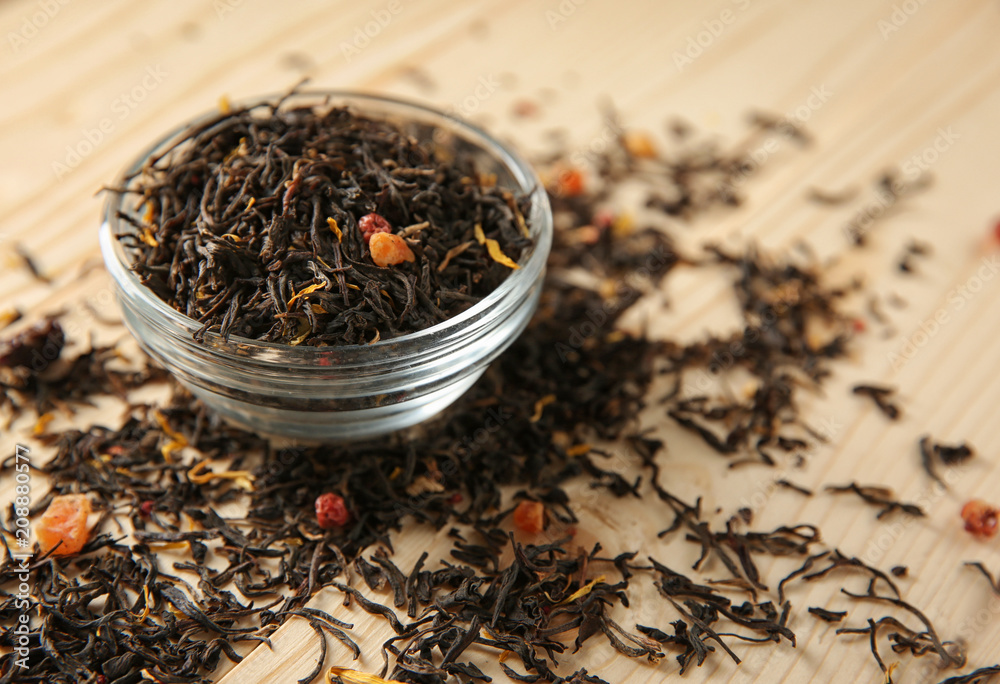 Glass bowl with dry tea leaves on wooden background