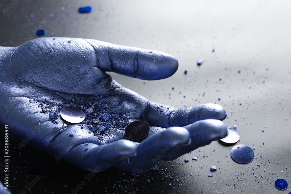 Purple human palm with sequins and powder on dark background