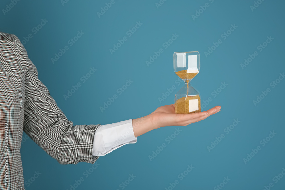 Woman holding hourglass on color background. Time management concept