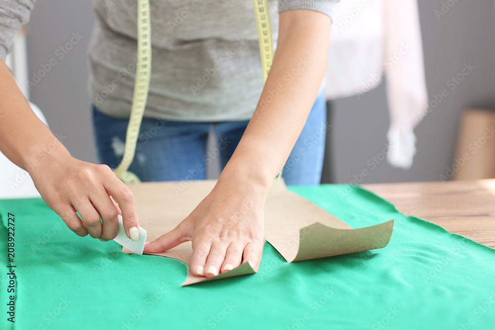 Young female tailor working with sewing pattern in atelier