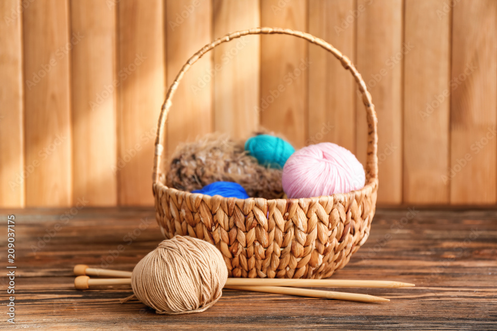 Wicker basket with knitting yarn and needles on table