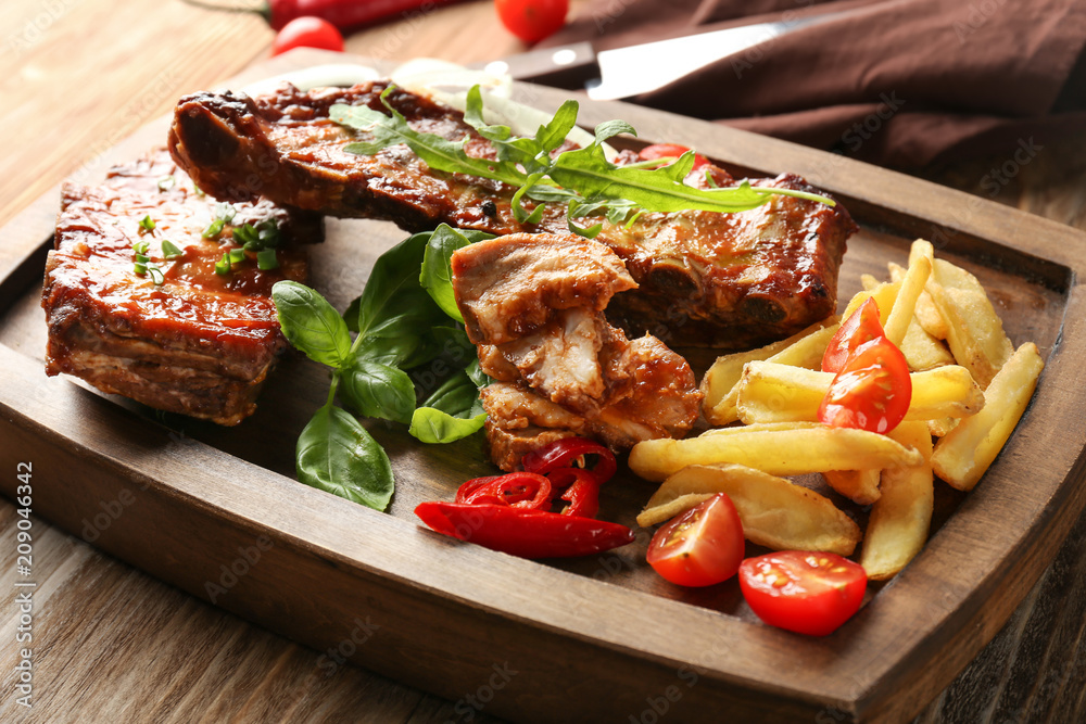 Wooden board with delicious grilled ribs and french fries on table