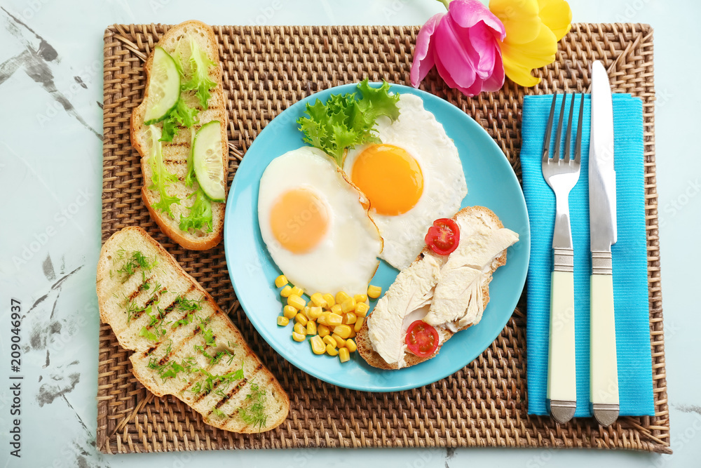 Plate with toasted bread, fried eggs and chicken on wicker mat