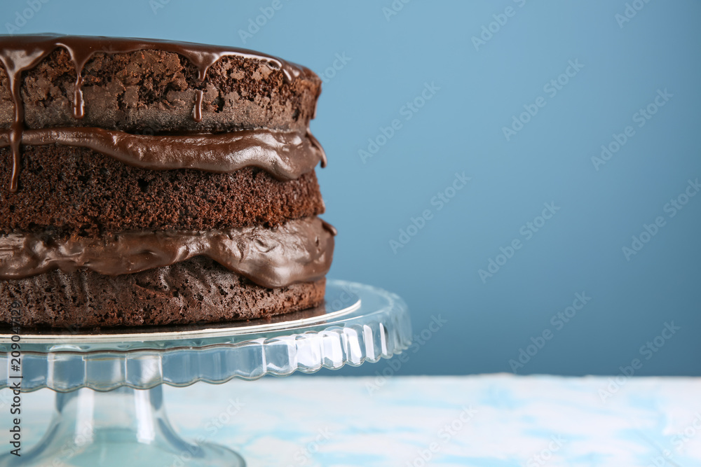 Dessert stand with delicious chocolate cake on table against color background