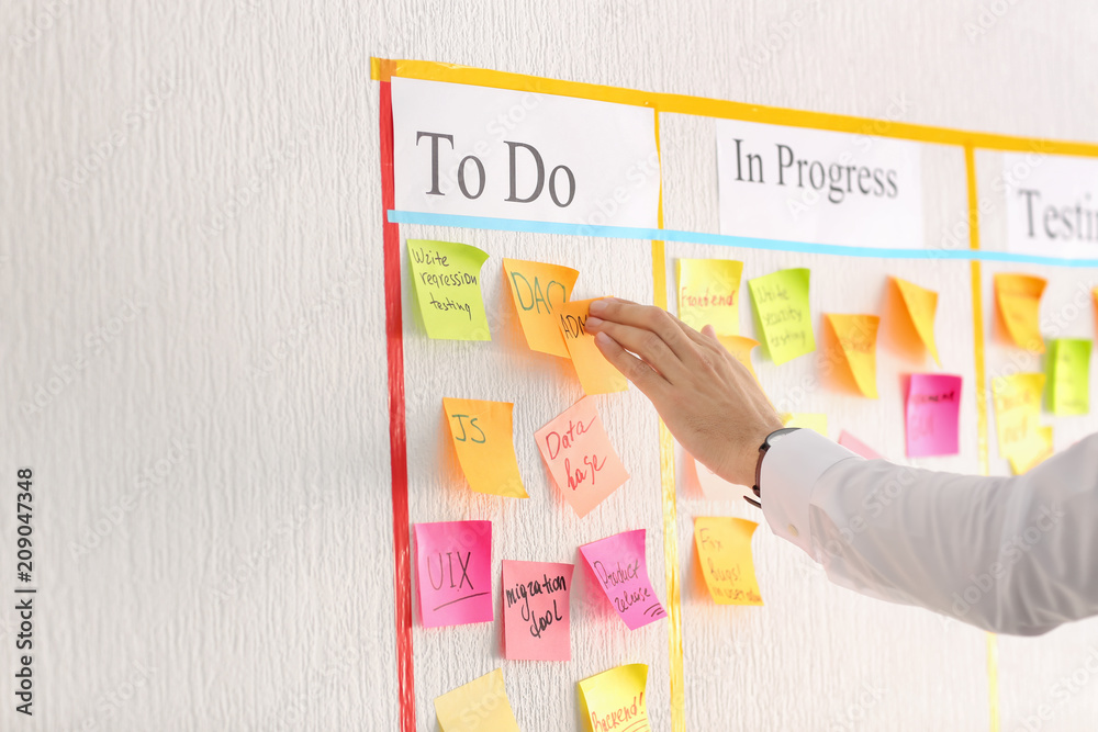 Man attaching sticky note to scrum task board in office