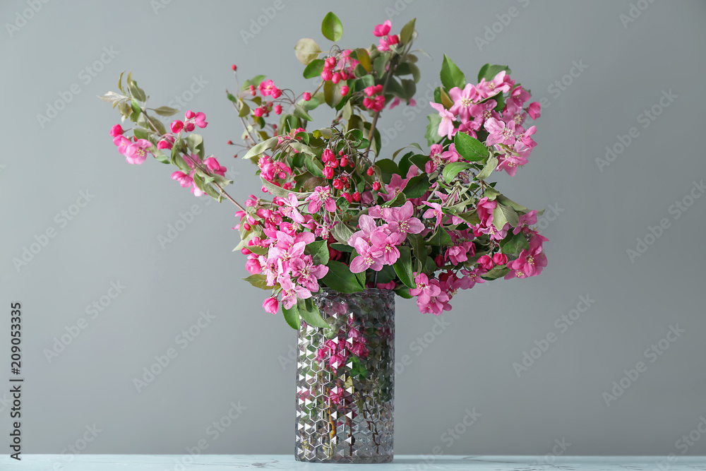 Vase with beautiful blossoming branches on grey background