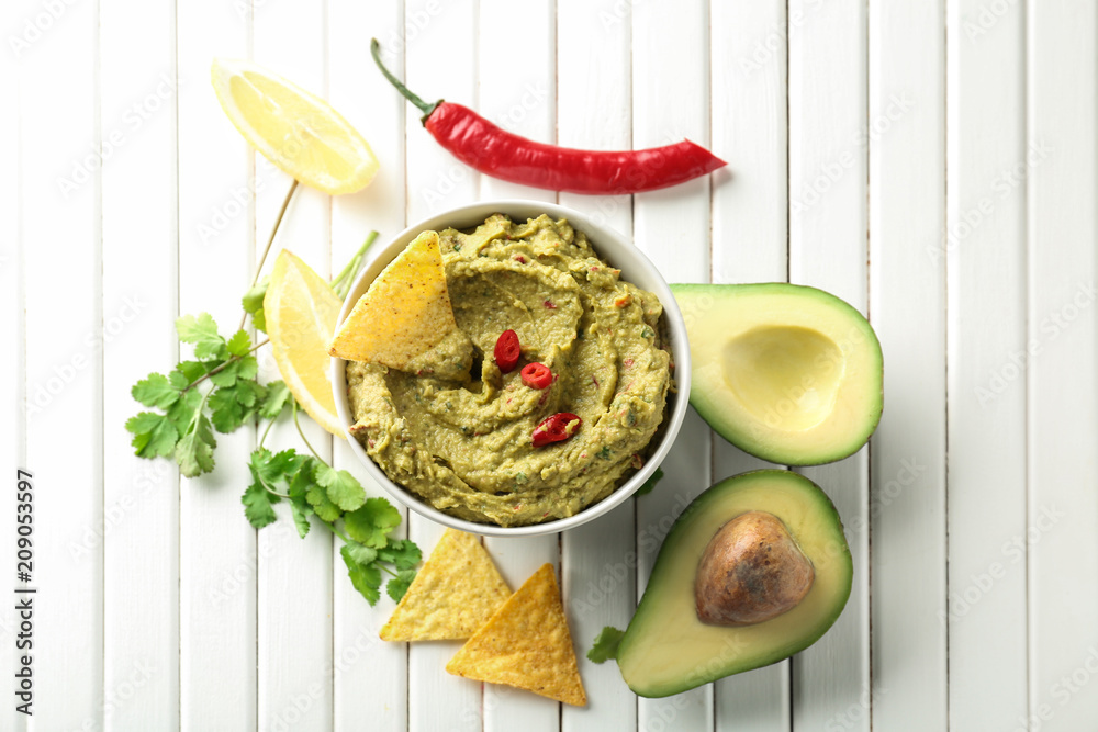 Bowl with delicious guacamole and nachos on wooden table