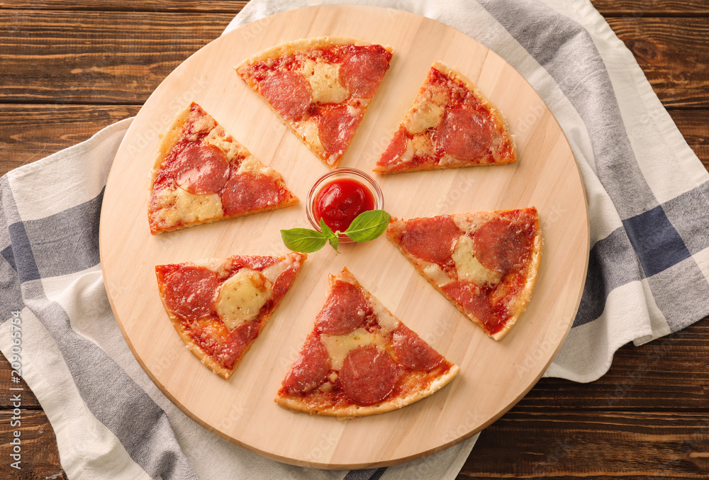 Wooden board with pieces of pepperoni pizza and sauce on table