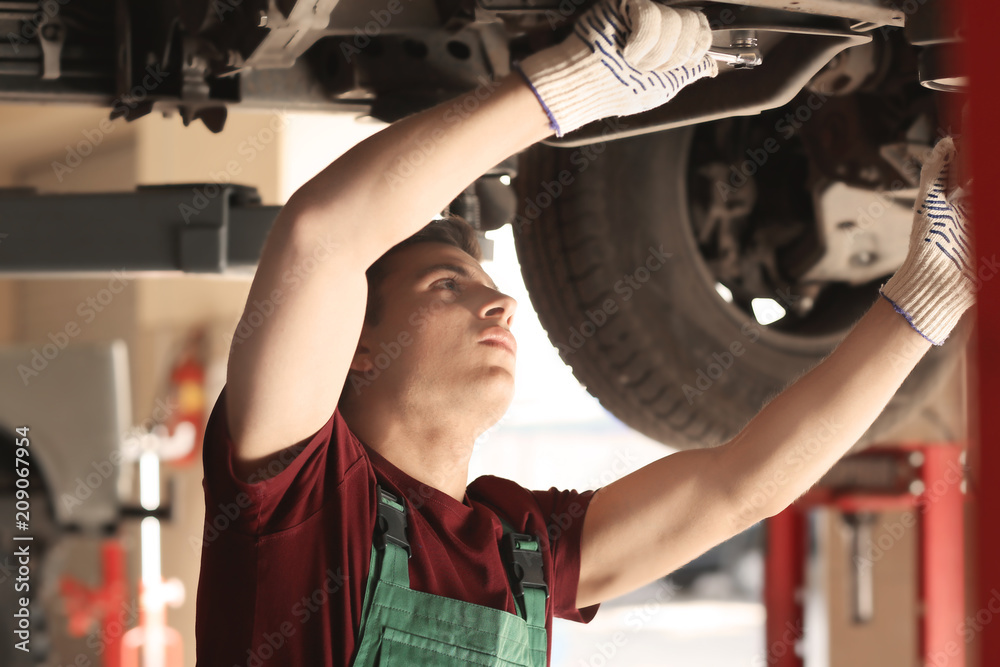 Young auto mechanic repairing car in service center