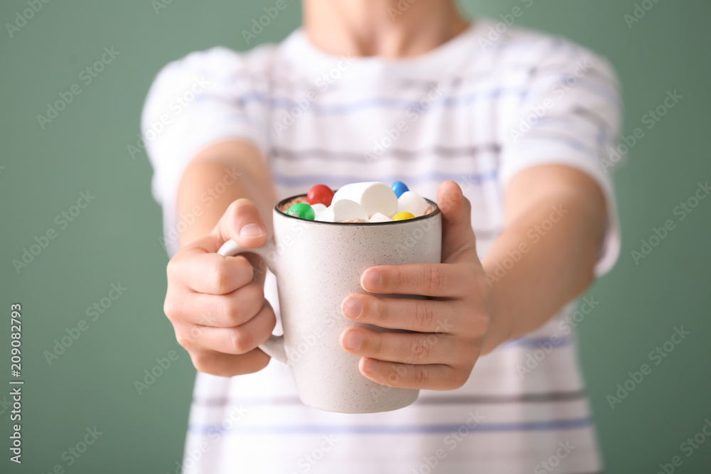 Cute little boy with cup of hot cocoa drink on color background, closeup