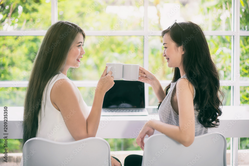 Two young Asian beautiful cheerful woman in sitting on coffee cafe laughing and drinking coffee from