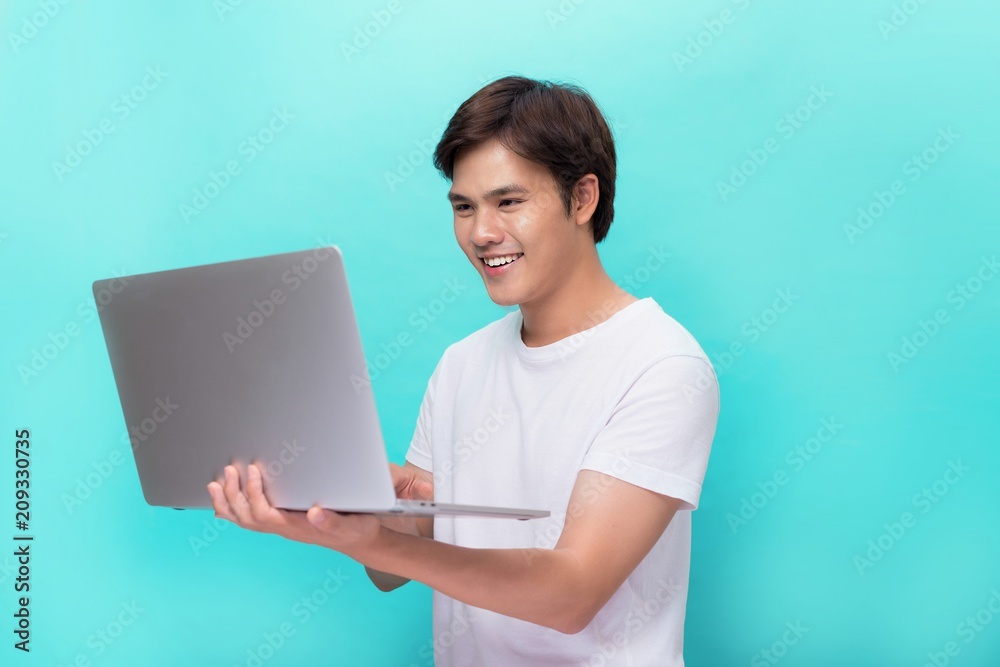 Portrait of smiling young man with laptop isolated on blue.