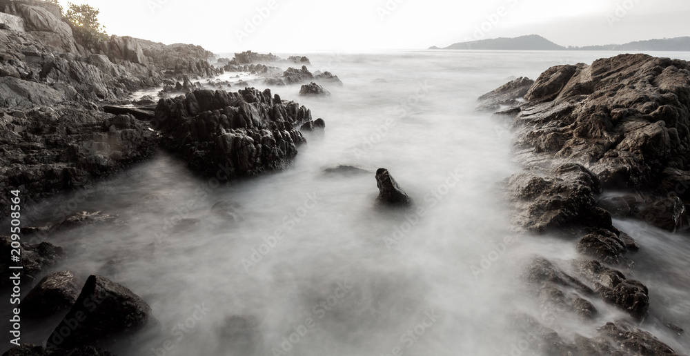 在日落景色背景下，岩石构成的戏剧性天空和海浪海景的长曝光图像。