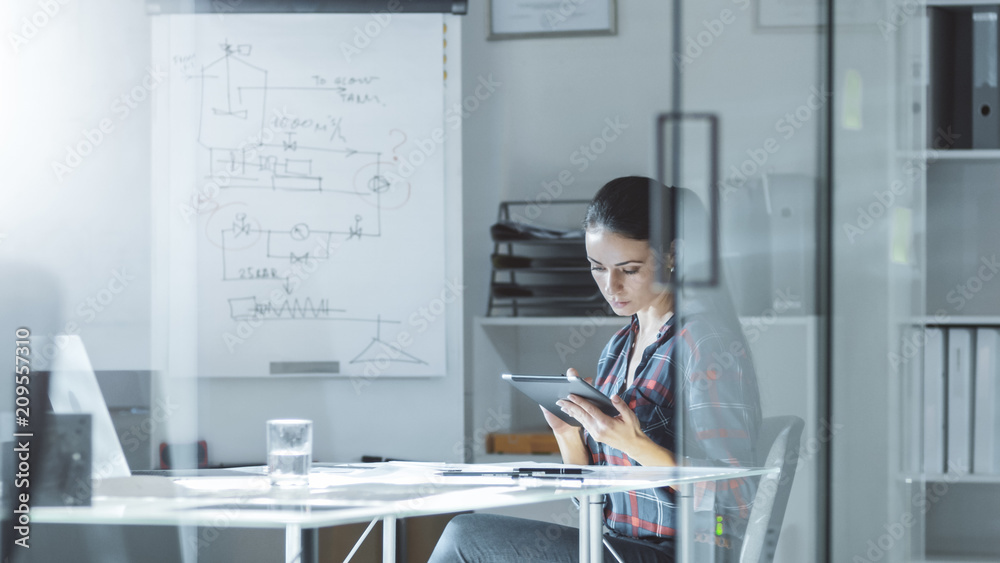 Female Design Engineer Sits at the Glass Table in Her Office, Works on a Tablet Computer, Blueprints