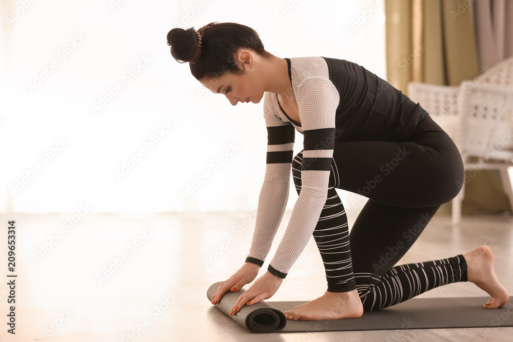 Beautiful woman with yoga mat indoors