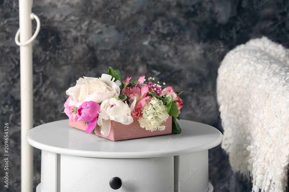 Box with beautiful flowers on beside table in room