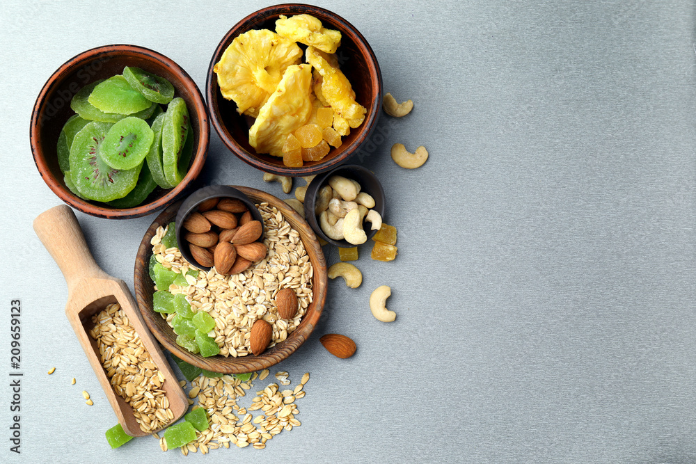 Bowls with oatmeal flakes, nuts and candied fruits on table, top view