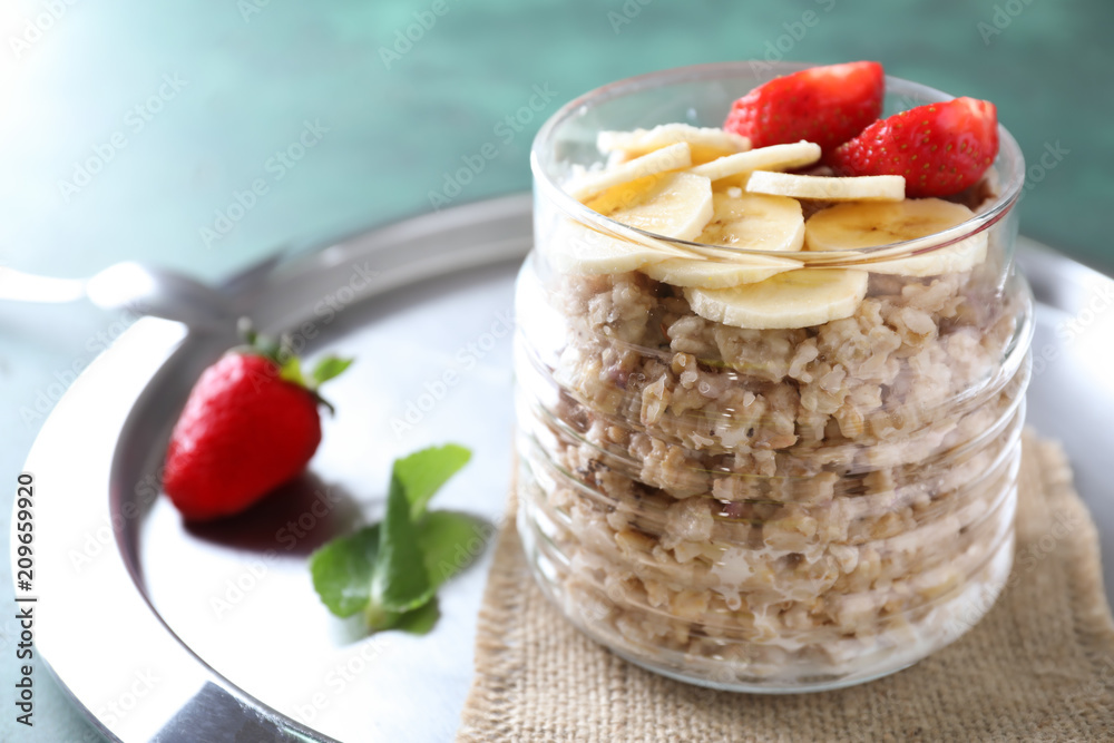 Glass jar with tasty oatmeal, sliced banana and strawberry on metal tray