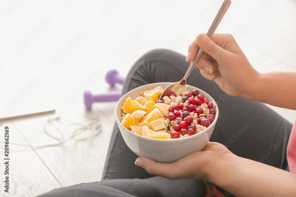 Sporty young woman sitting on floor with bowl of tasty oatmeal