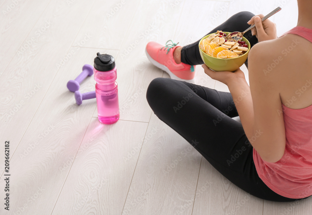 Sporty young woman sitting on floor with bowl of tasty oatmeal