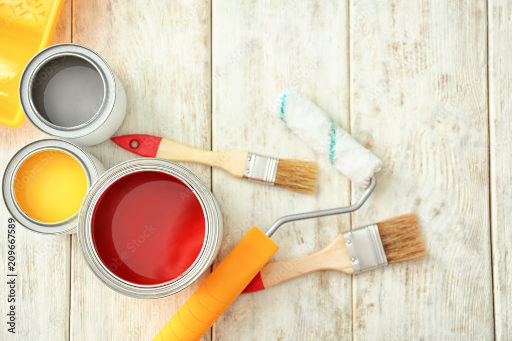 Cans of paint, roller and brushes on wooden background