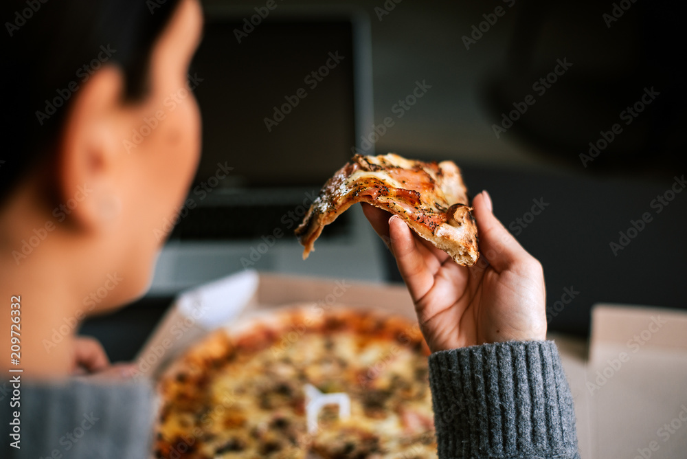 Rear view of woman taking a slice of pizza.