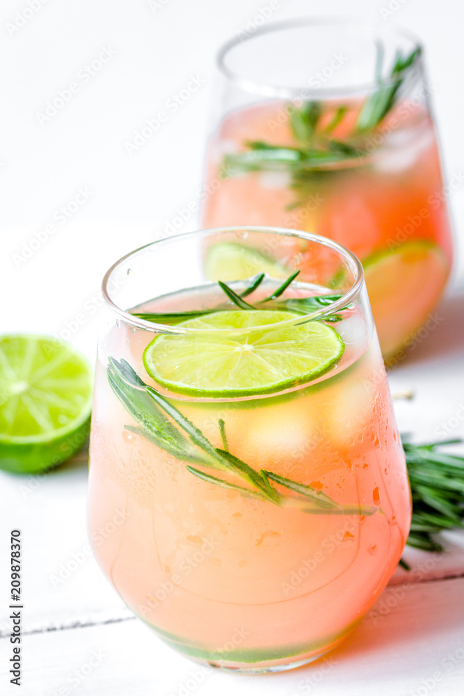 sliced lime, rosemary and natural juice in glass on white table 