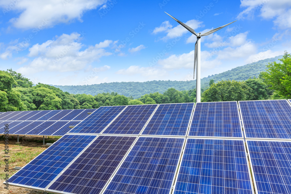 Solar panels and wind turbines with mountains landscape under the blue sky